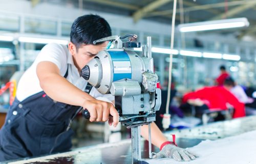 Indonesian worker using a cutter - a large machine for cutting fabrics - in a asian textile factory, he wears a chain glove