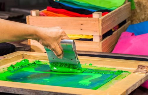 hand made screen printing tee shirt in love design. put block screen print of green color on tee shirt put green ink on block screen the press green ink by rubber handle